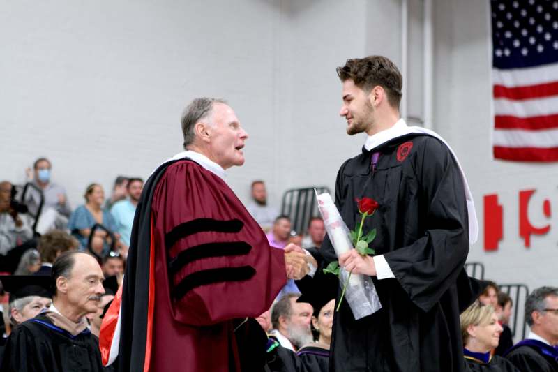 a man in a graduation gown holding a rose and another man in a robe