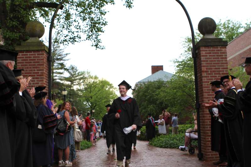 a man in a graduation gown and cap walking down a brick path