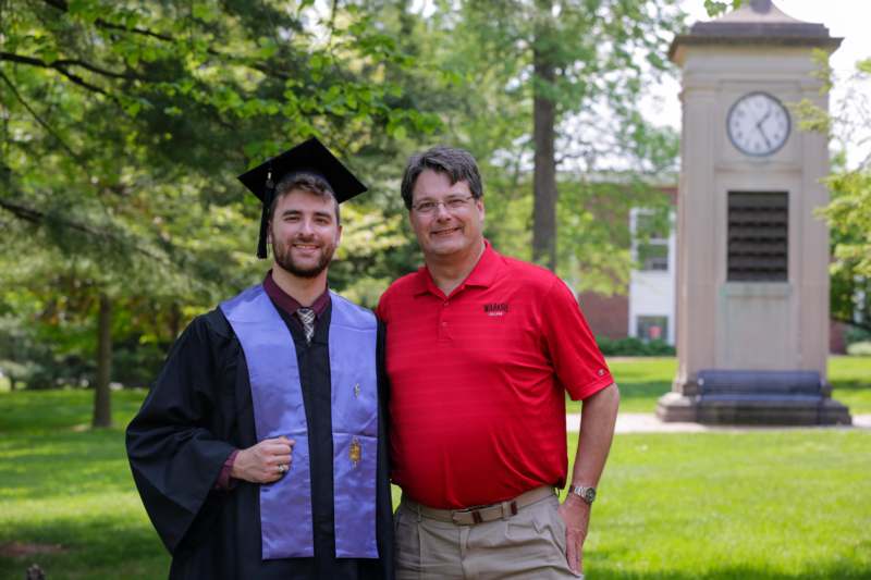 a man in a graduation gown and cap standing next to a man in a red shirt