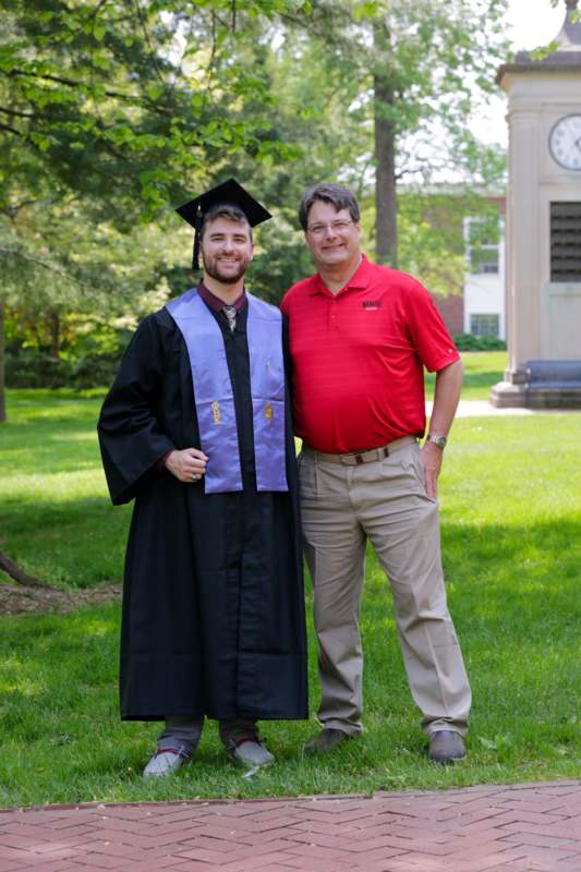 a man in a graduation gown and cap standing next to a man in a red shirt