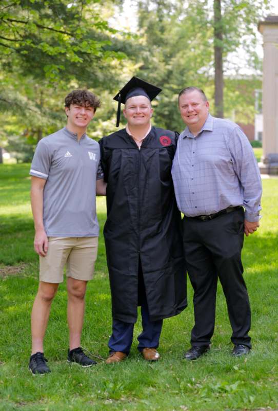 a man in a graduation gown and cap standing with two men