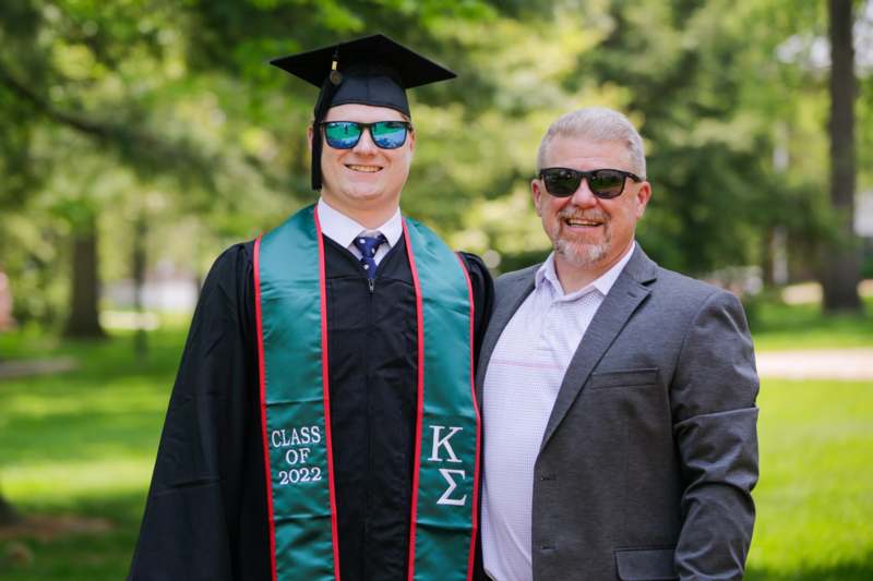 a man in a graduation cap and gown standing next to a man in sunglasses