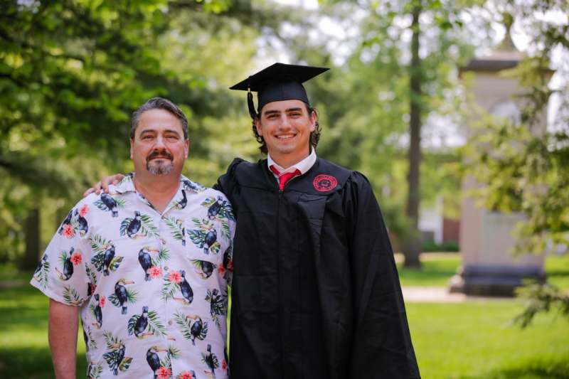 a man in a graduation gown and cap standing next to a man in a hawaiian shirt