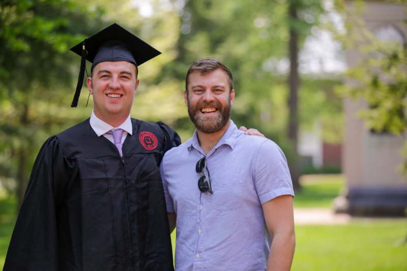 a man in a graduation gown and cap standing next to another man