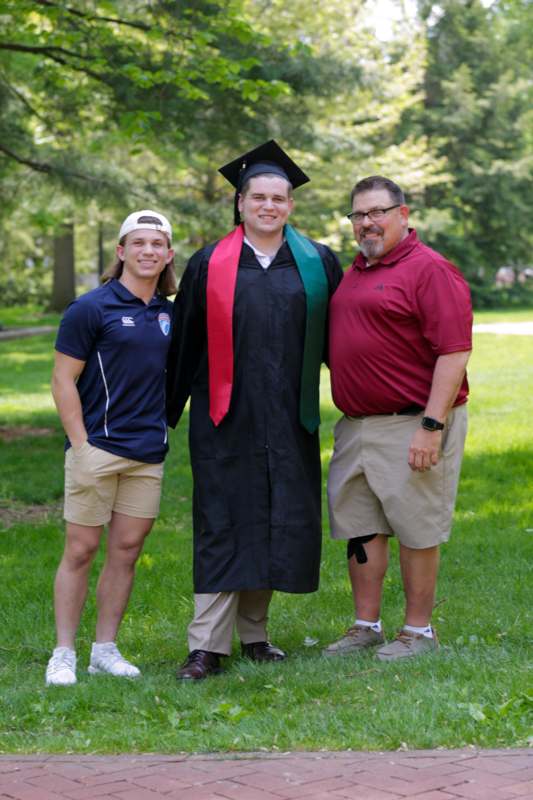 a man in a graduation gown and cap standing with two men