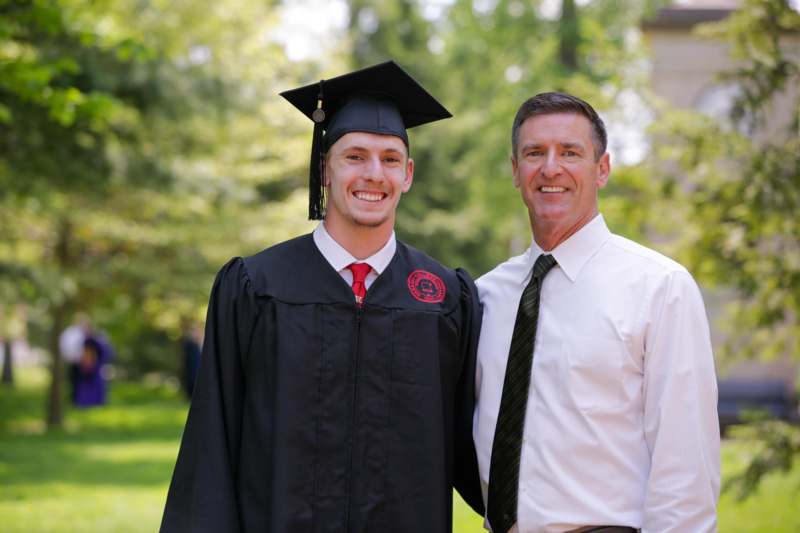a man in a graduation gown and cap standing next to a man in a white shirt