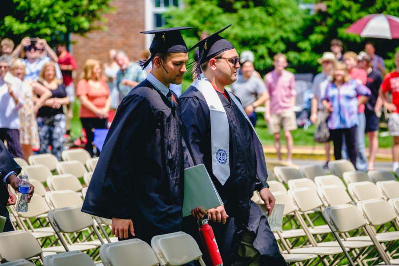 a group of men in graduation gowns and caps walking in chairs