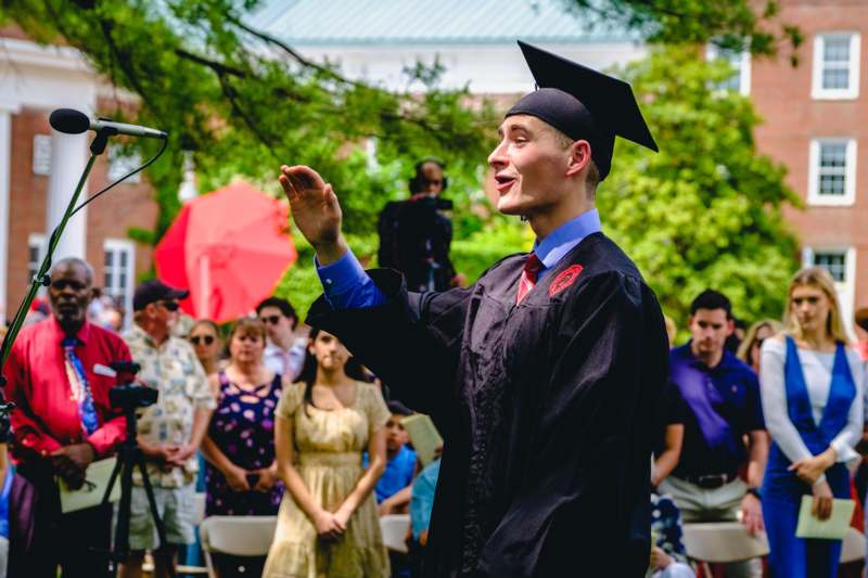 a man in a graduation gown and cap standing in front of a crowd