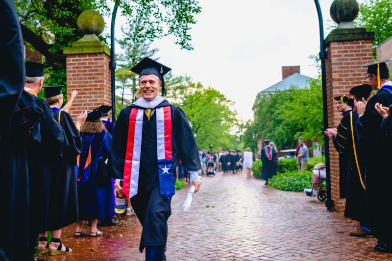 a man in a graduation gown and cap walking down a brick path
