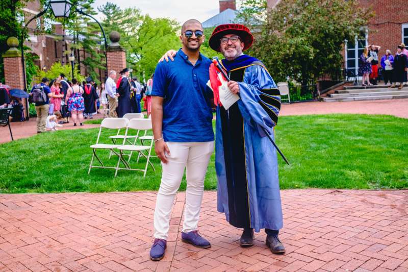 a man in a robe and hat standing next to a man in a graduation gown
