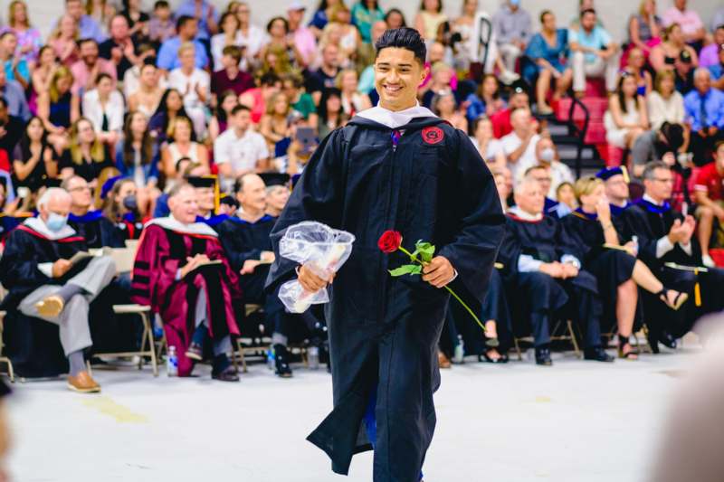 a man in a graduation gown holding a rose and a bouquet of flowers