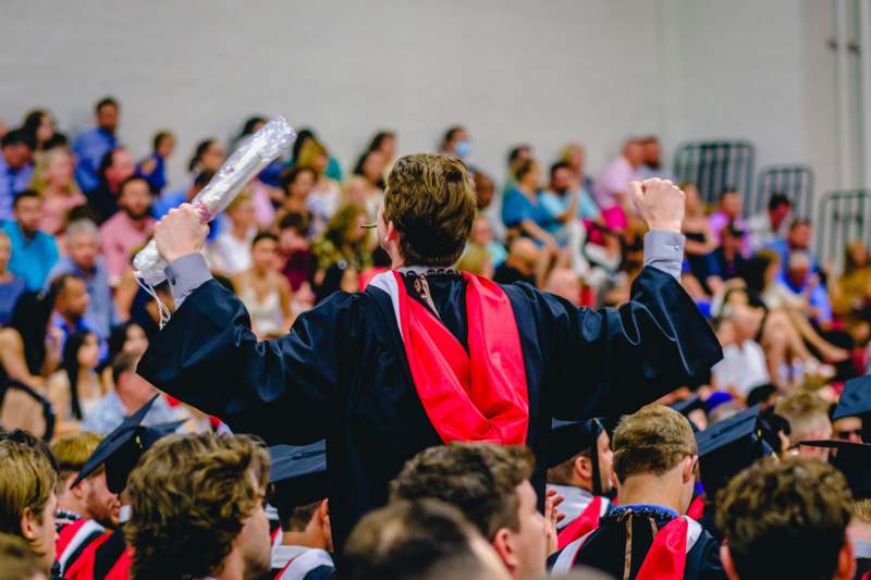 a man in a graduation gown raising his fist up