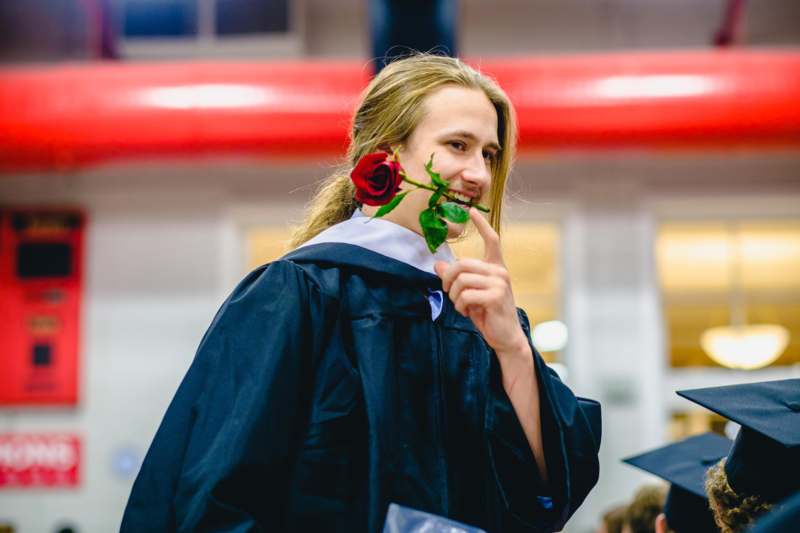 a man in a graduation gown holding a rose in his mouth