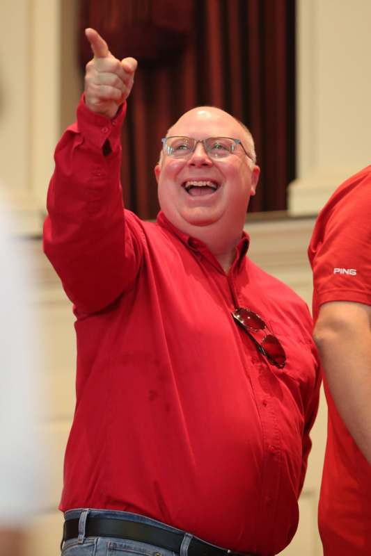 a man in red shirt with glasses and a red shirt pointing up