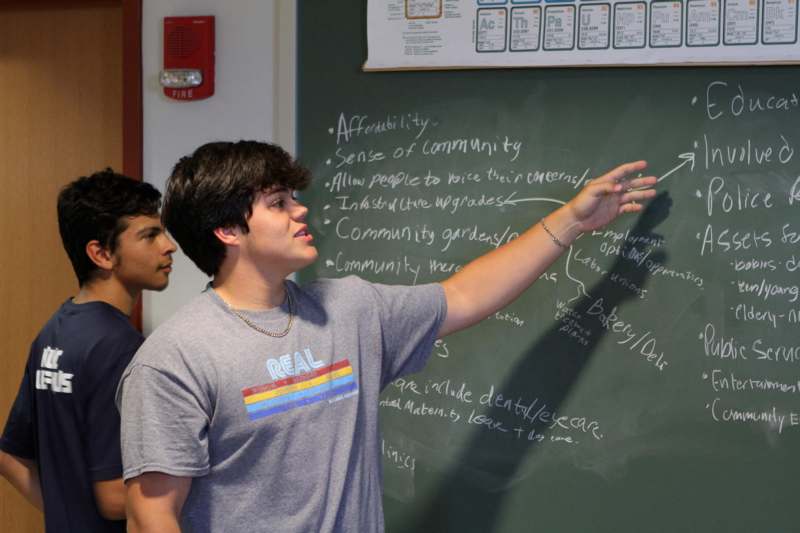 a young man pointing at a chalkboard
