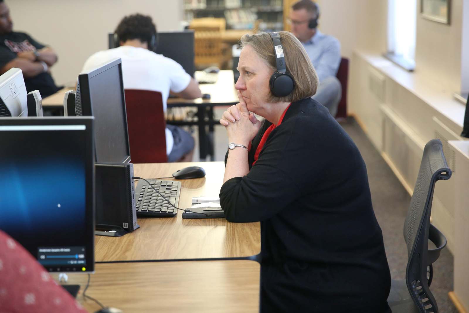 a woman wearing headphones sitting at a desk with other people in the background