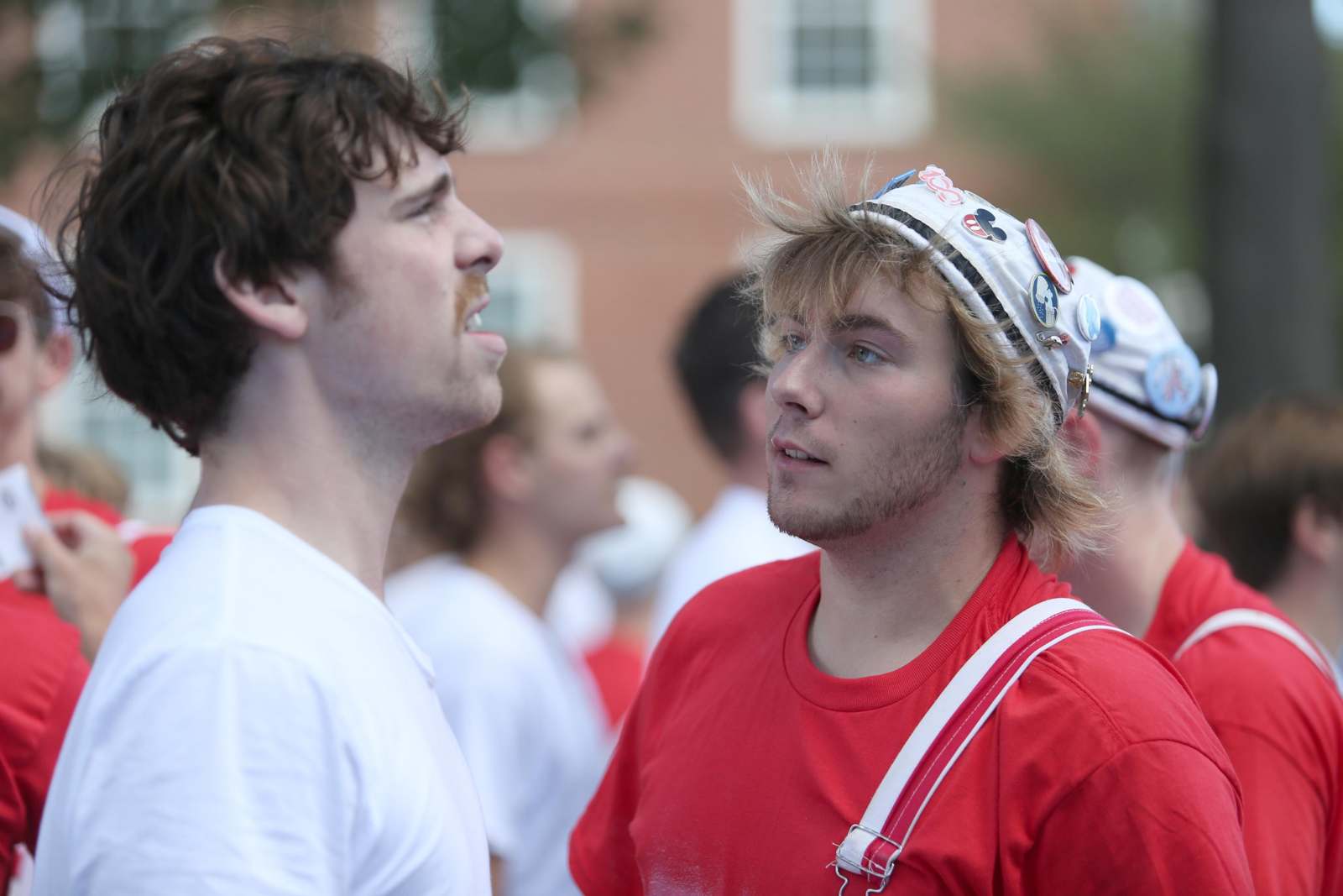a man in a red shirt and a white hat looking at another man