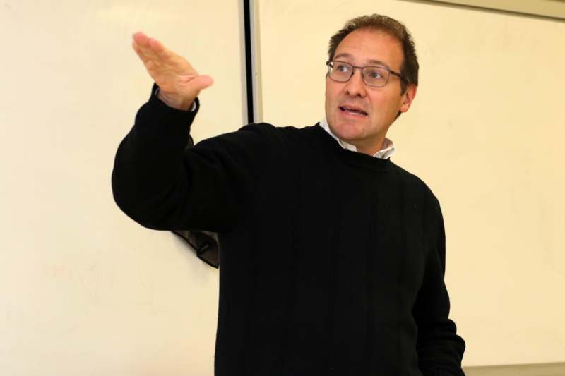 a man wearing glasses and a black sweater holding his hand up