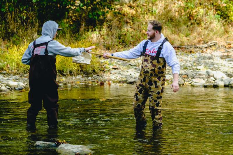 a man in a suit holding a stick to another man in a river