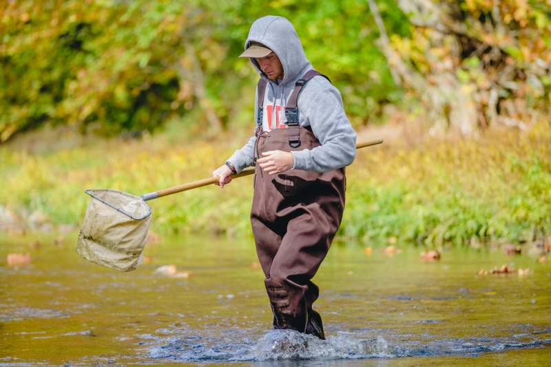 a man in overalls holding a net in a river
