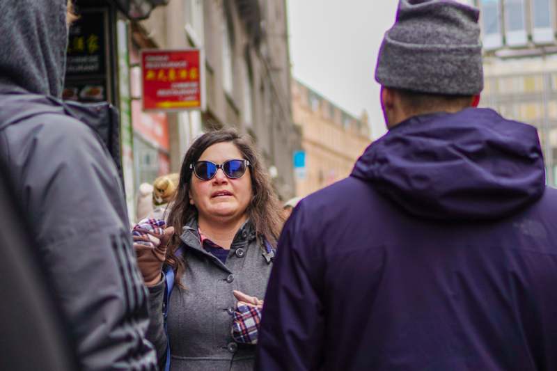 a woman wearing sunglasses and a grey coat standing on a street