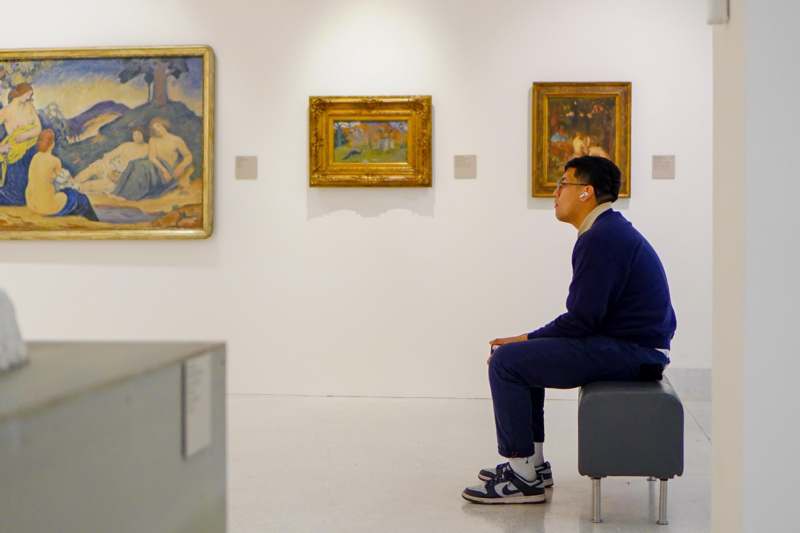 a man sitting on a bench in front of paintings