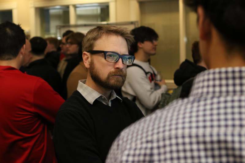 a man with glasses and a beard in a room with other people