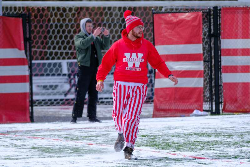a man in red and white striped pants and a red hat walking on snow