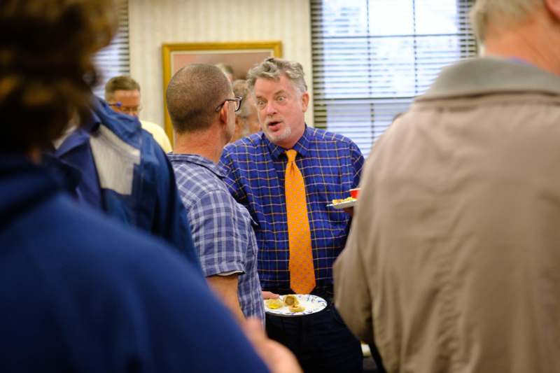a man in a blue shirt and orange tie talking to a group of people