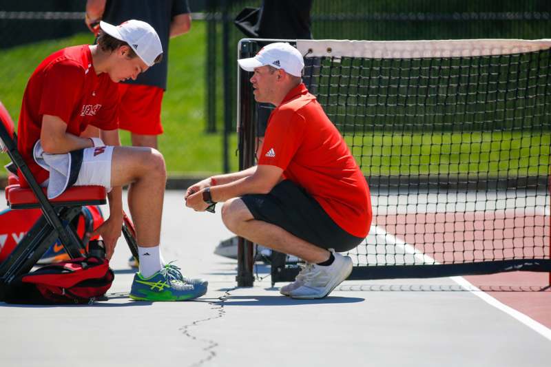 a man kneeling next to another man on a tennis court