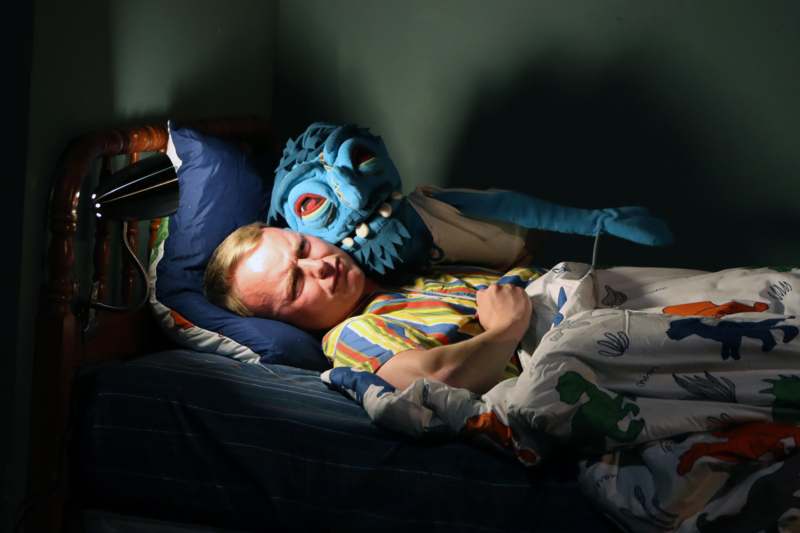 a man lying in bed with a blue monster mask
