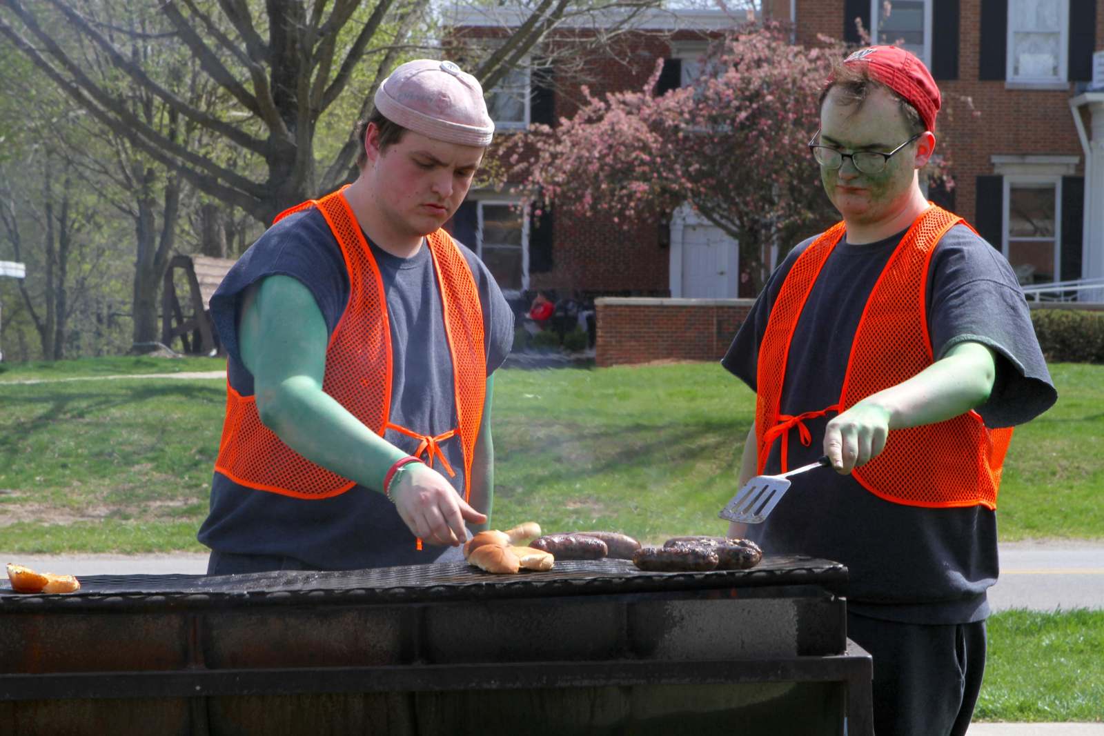 a group of men wearing orange vests cooking food on a grill