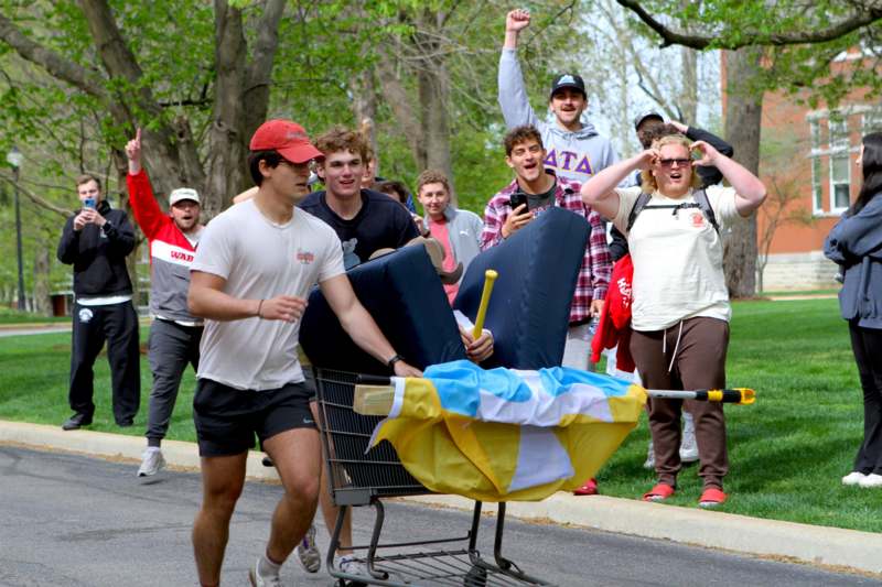 a group of people running with a cart full of objects