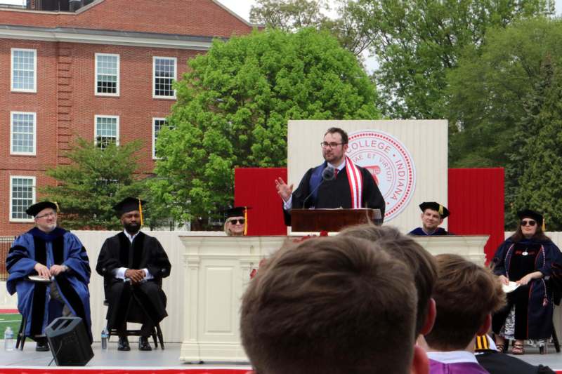 a man in a graduation cap and gown speaking at a podium
