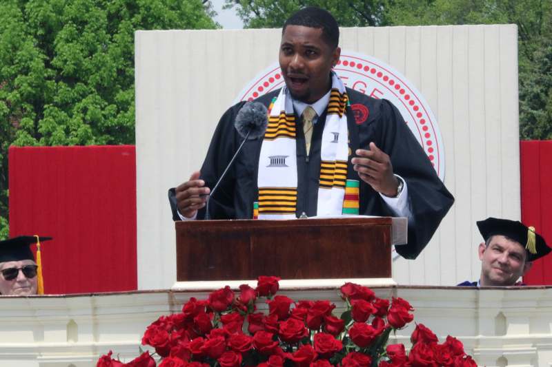 a man in a graduation gown speaking into a microphone