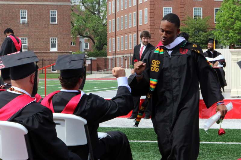a man in a graduation gown and cap shaking hands with other people