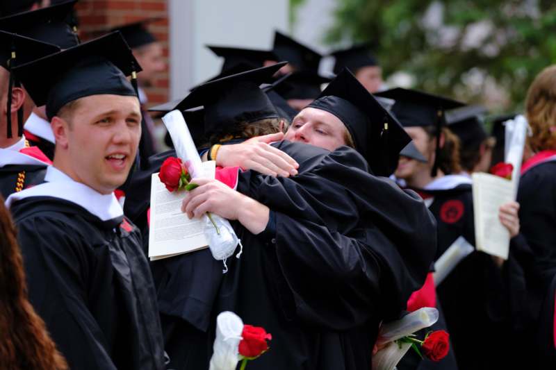 a group of people in graduation gowns and caps hugging