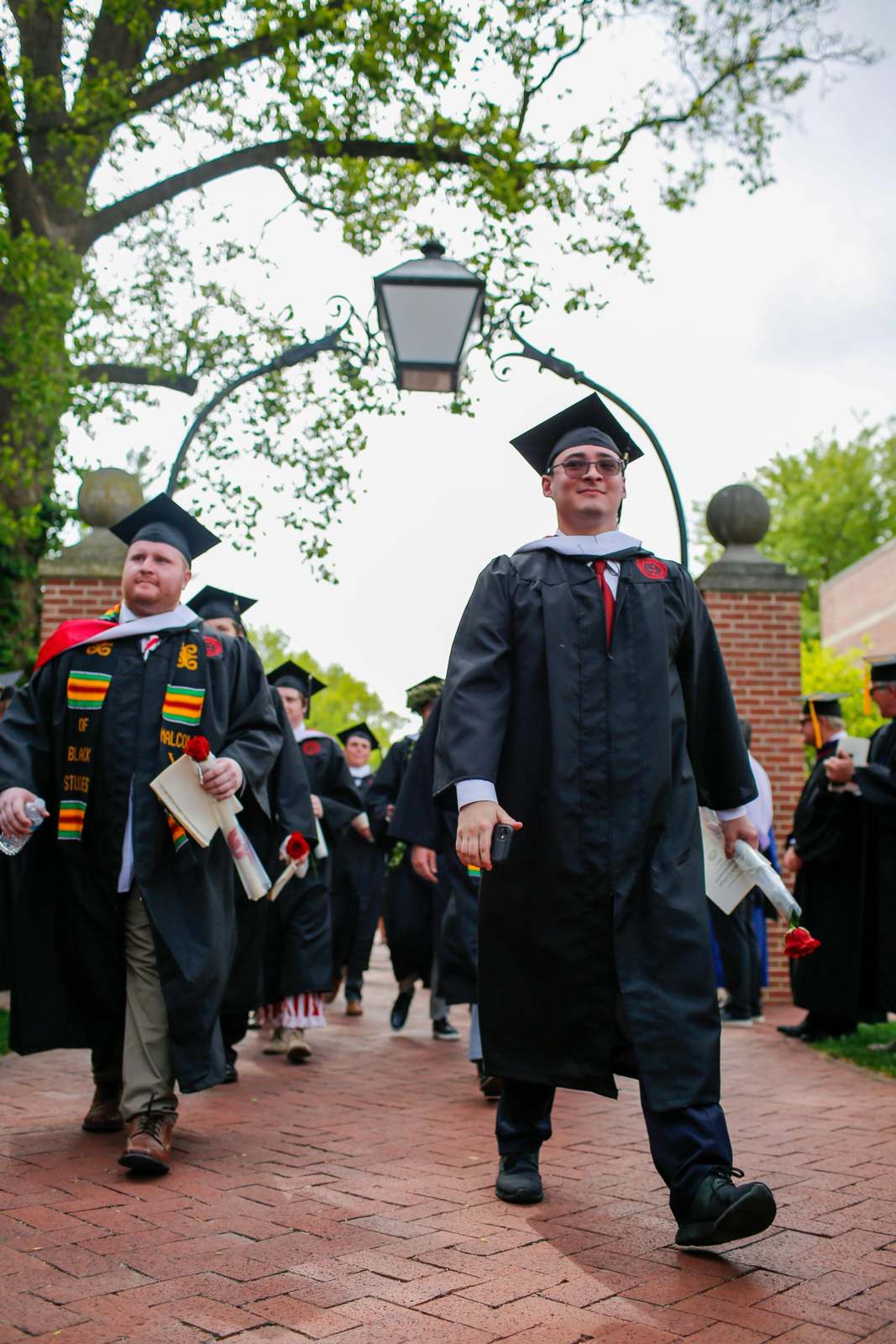 a group of people in graduation gowns and caps walking down a brick path
