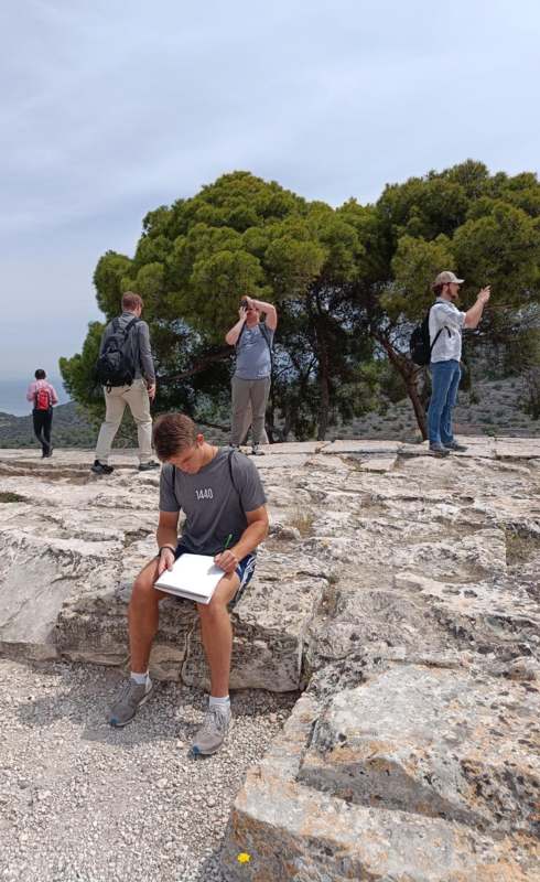 a man sitting on a rock with a book and a group of people