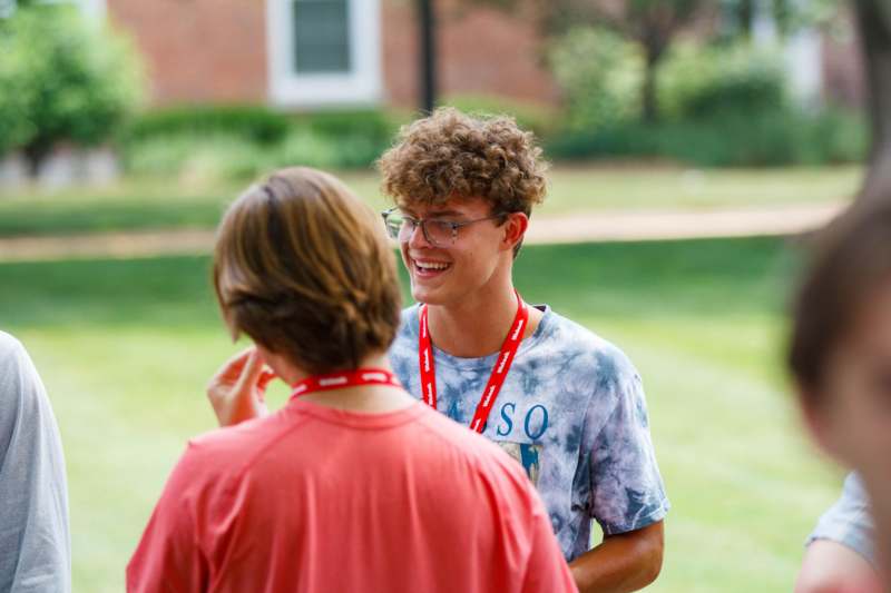 a man in glasses and a red lanyard talking to another man
