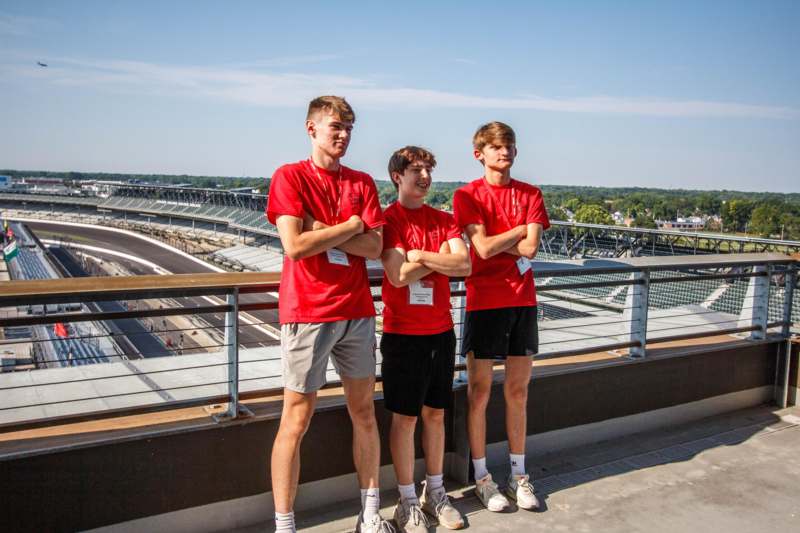a group of boys standing on a balcony with a railing and a stadium