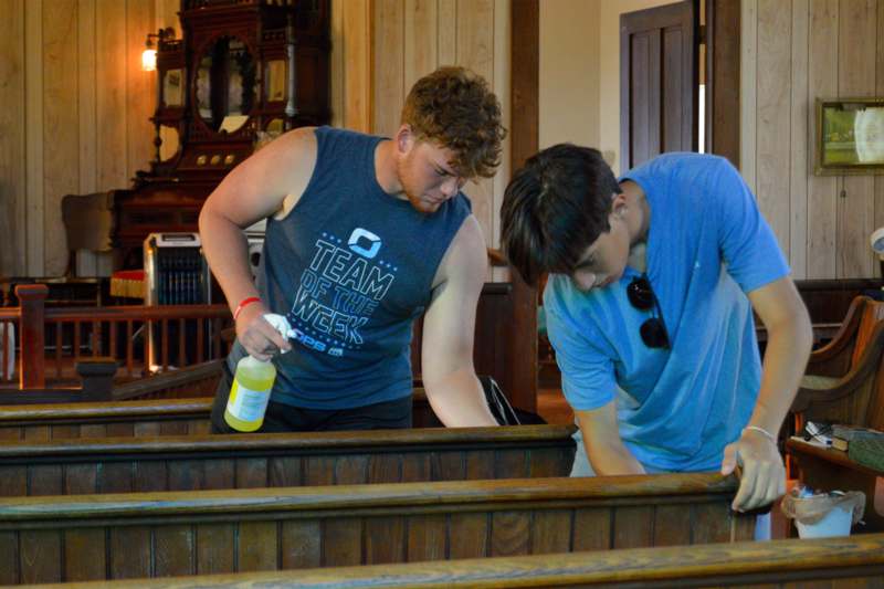 two men spraying a bottle of liquid on pews