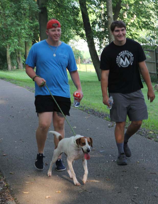 two men walking a dog on a path