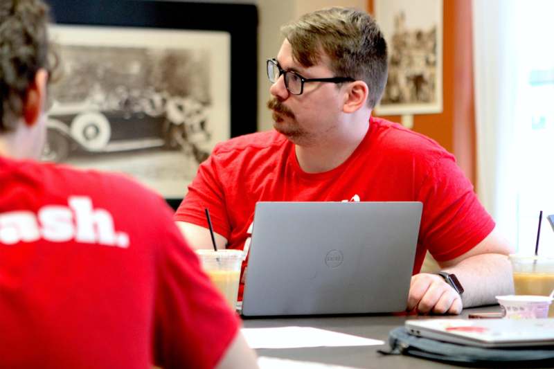 a man in red shirt sitting at a table with a laptop