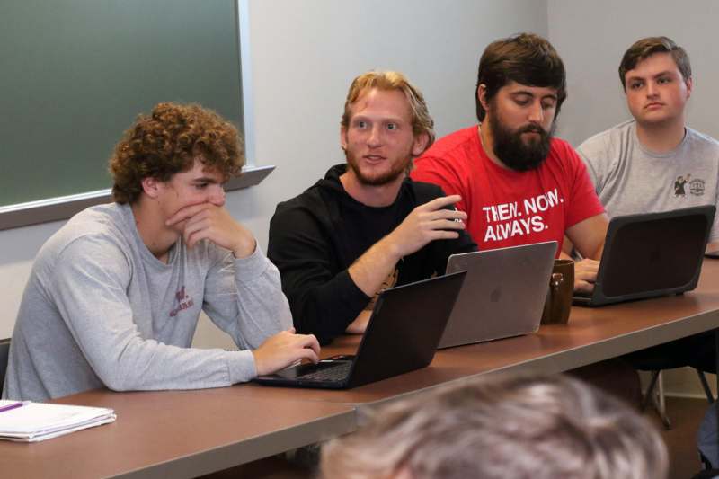 a group of men sitting at a table with laptops