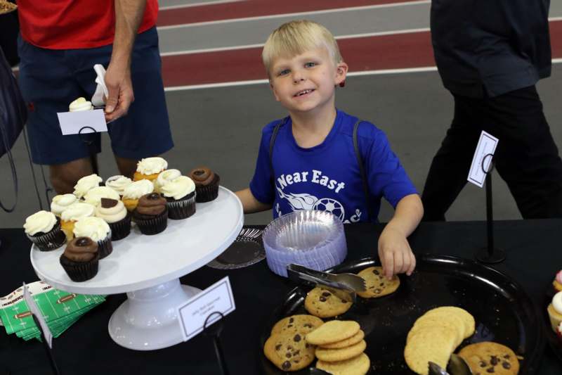 a boy sitting at a table with cookies and cupcakes