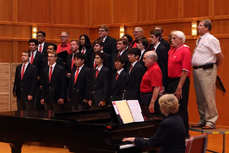 a group of people in suits and ties standing in front of a piano