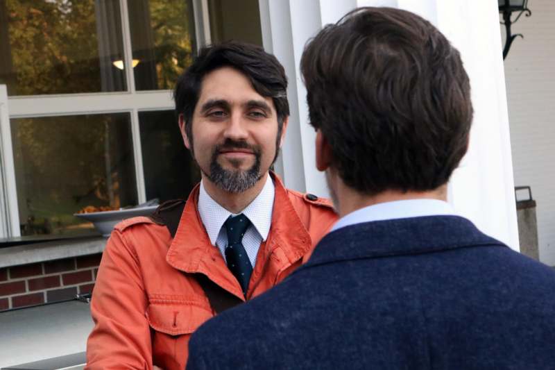 a man in an orange jacket and tie talking to another man