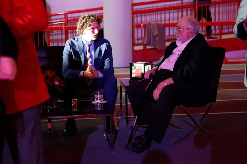 a man in a suit sitting in a chair next to a man in a suit