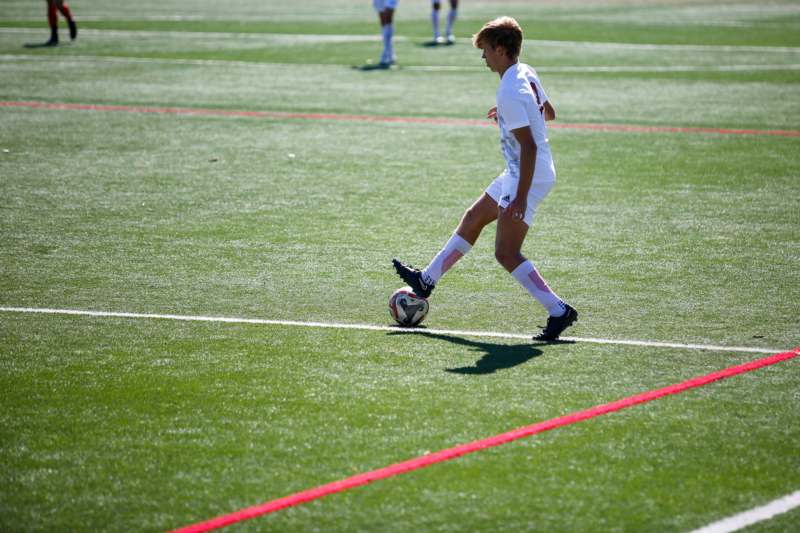 a boy in a white uniform kicking a football ball on a field